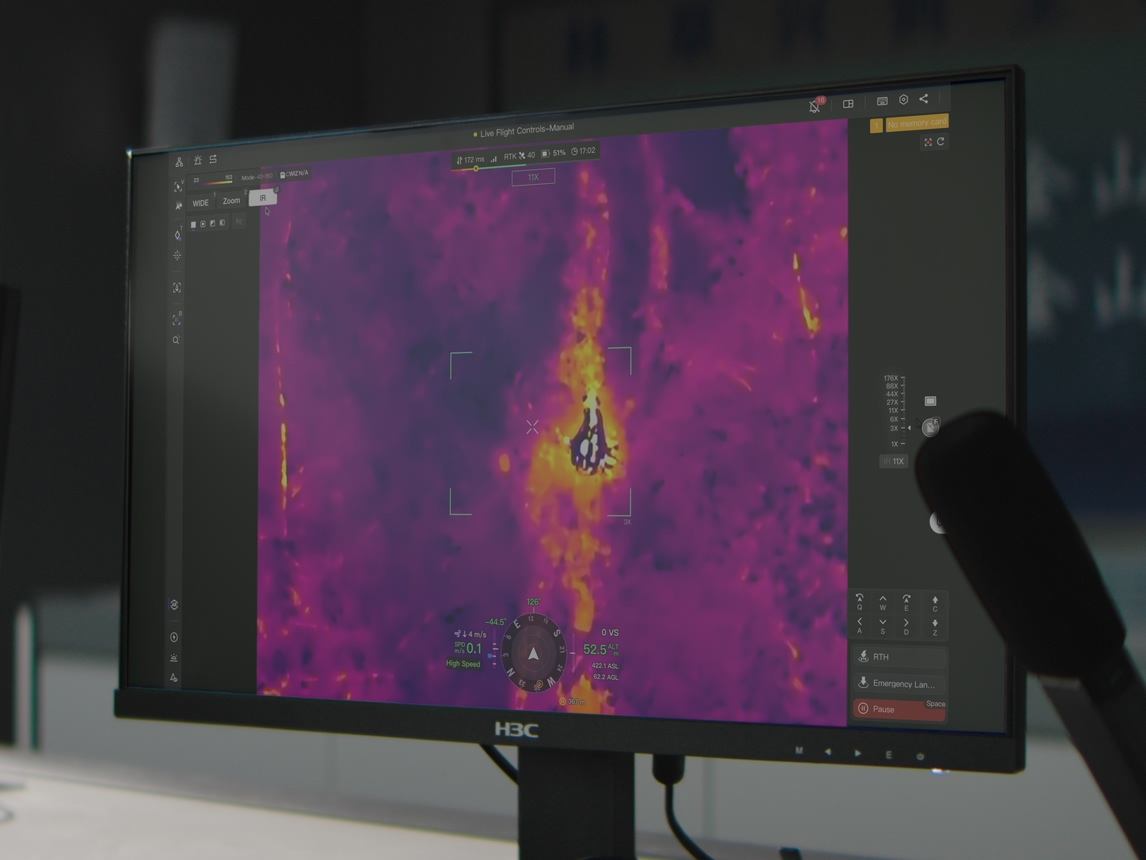 Radiometric thermal drone feed showing a heat source on a monitor in an operations room, from official DJI imagery.