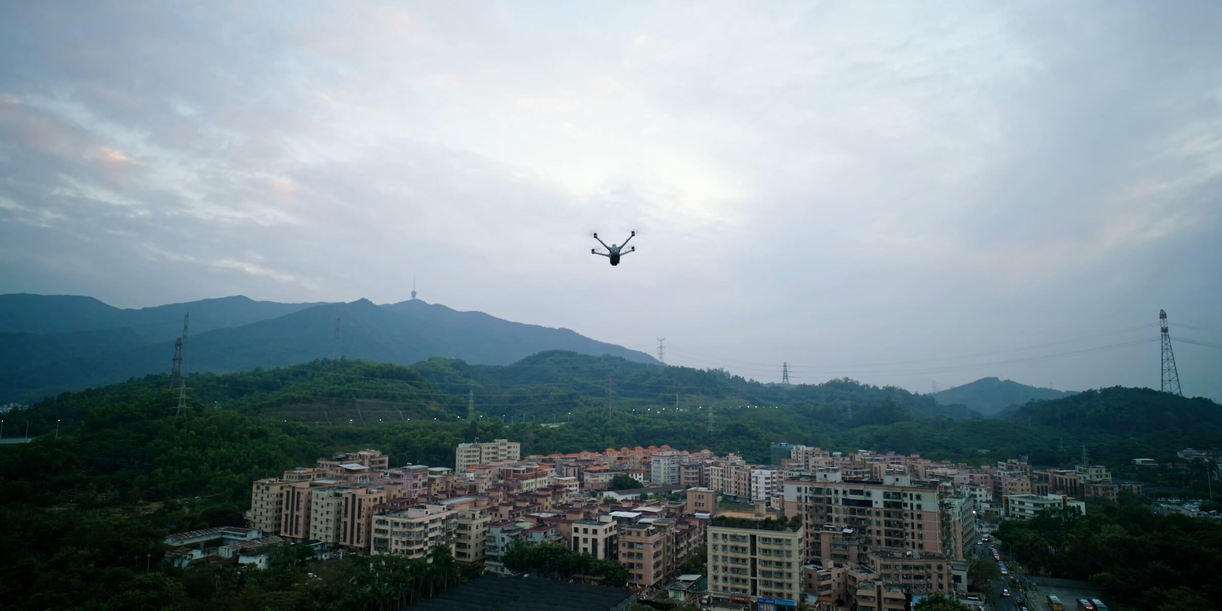 DJI dock drone in flight under open sky above a town and hills.