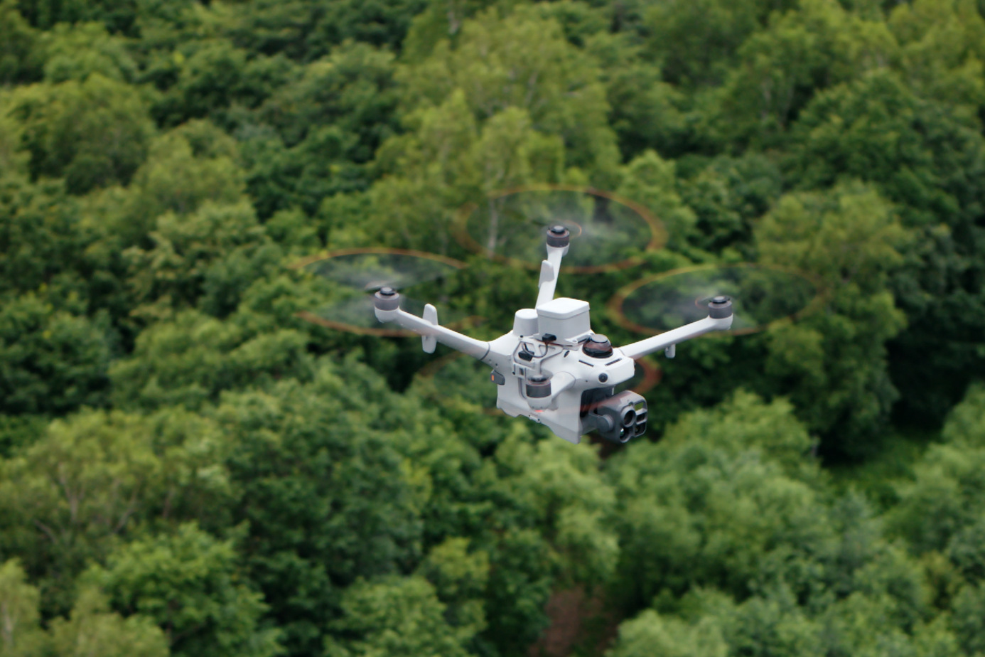 DJI enterprise drone flying low over a dense forest canopy, from official DJI Dock 4 imagery.
