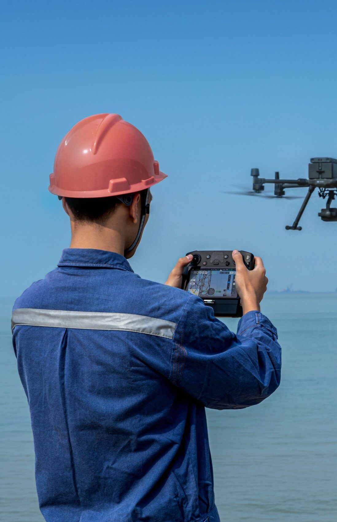Construction worker in a hard hat operating a DJI enterprise drone from a handheld controller on site.
