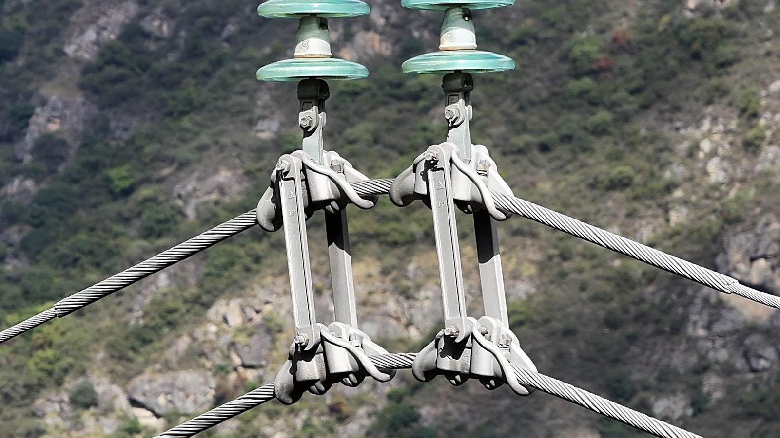 Close-up drone view of conductor clamps, splices, and glass insulators on an energized transmission line.