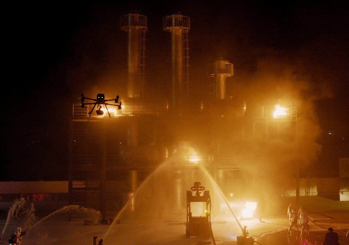 Enterprise drone flying a night inspection over an illuminated industrial facility.