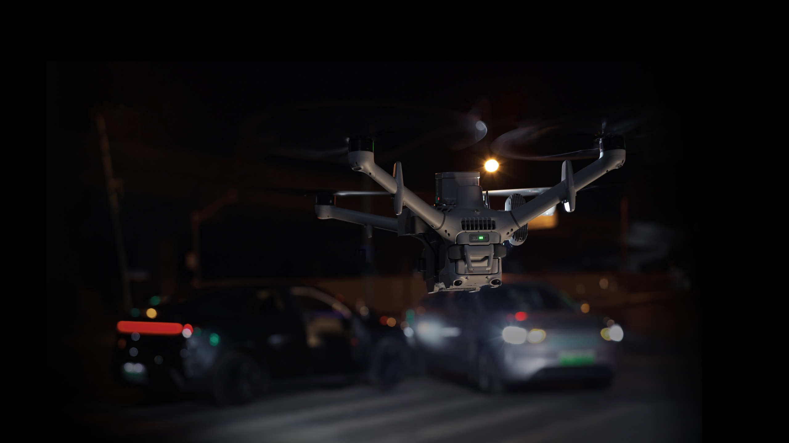 DJI Matrice 5TD with a spotlight flying a night patrol over a parking area, from official DJI imagery.