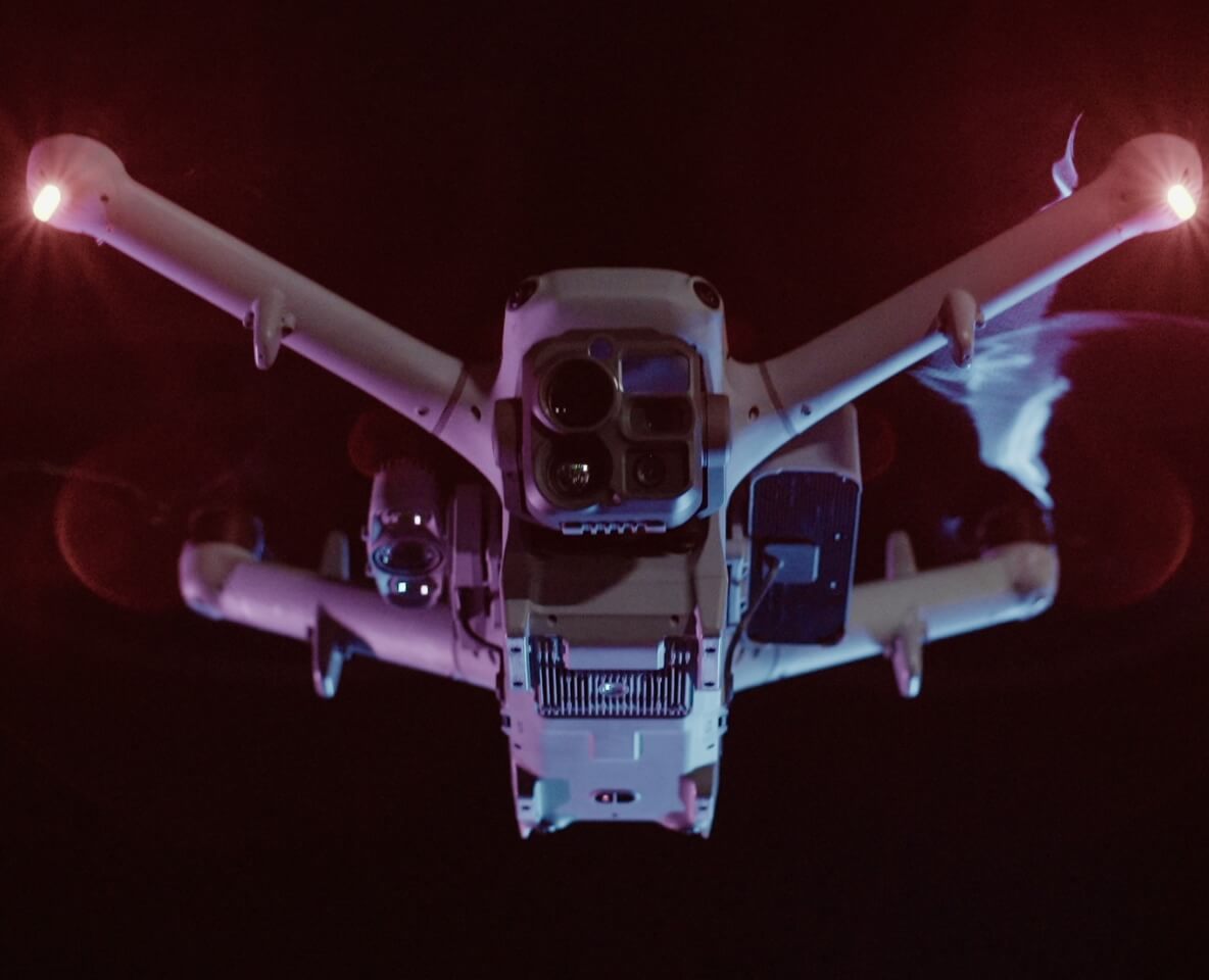 DJI Matrice 5TD flying at night, viewed from below with its infrared camera visible.