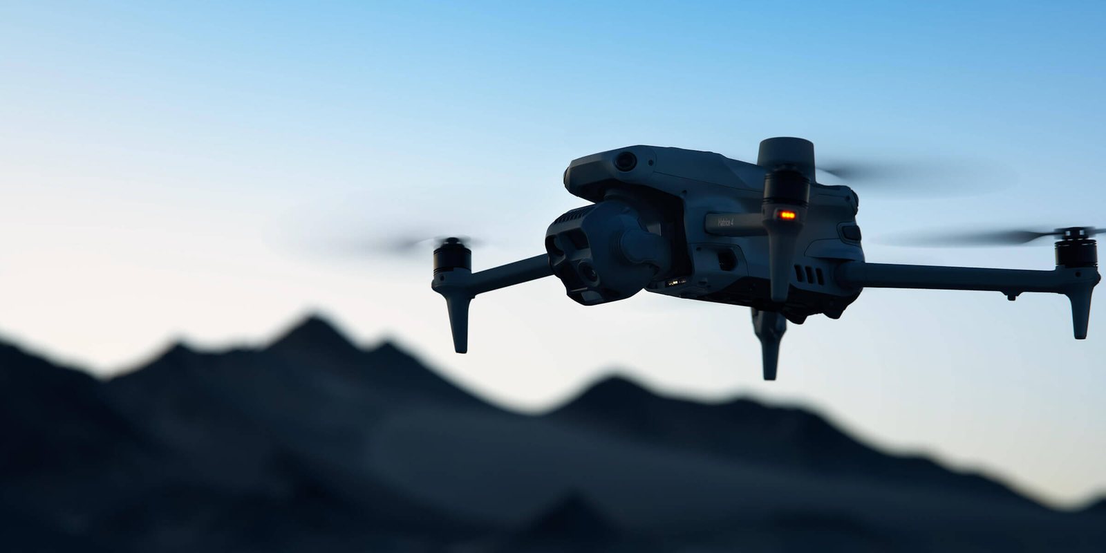 DJI Matrice 4T thermal inspection drone in flight at dusk with mountains behind it.