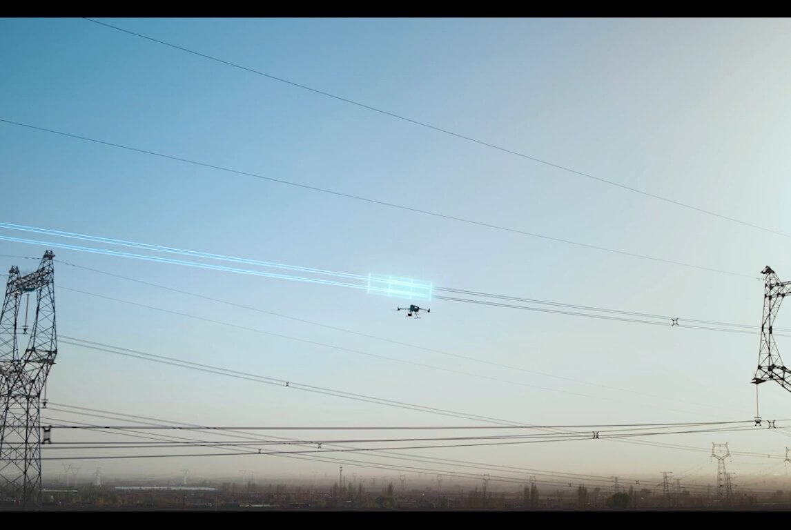 DJI enterprise drone flying along energized transmission conductors between two lattice towers during a powerline inspection.
