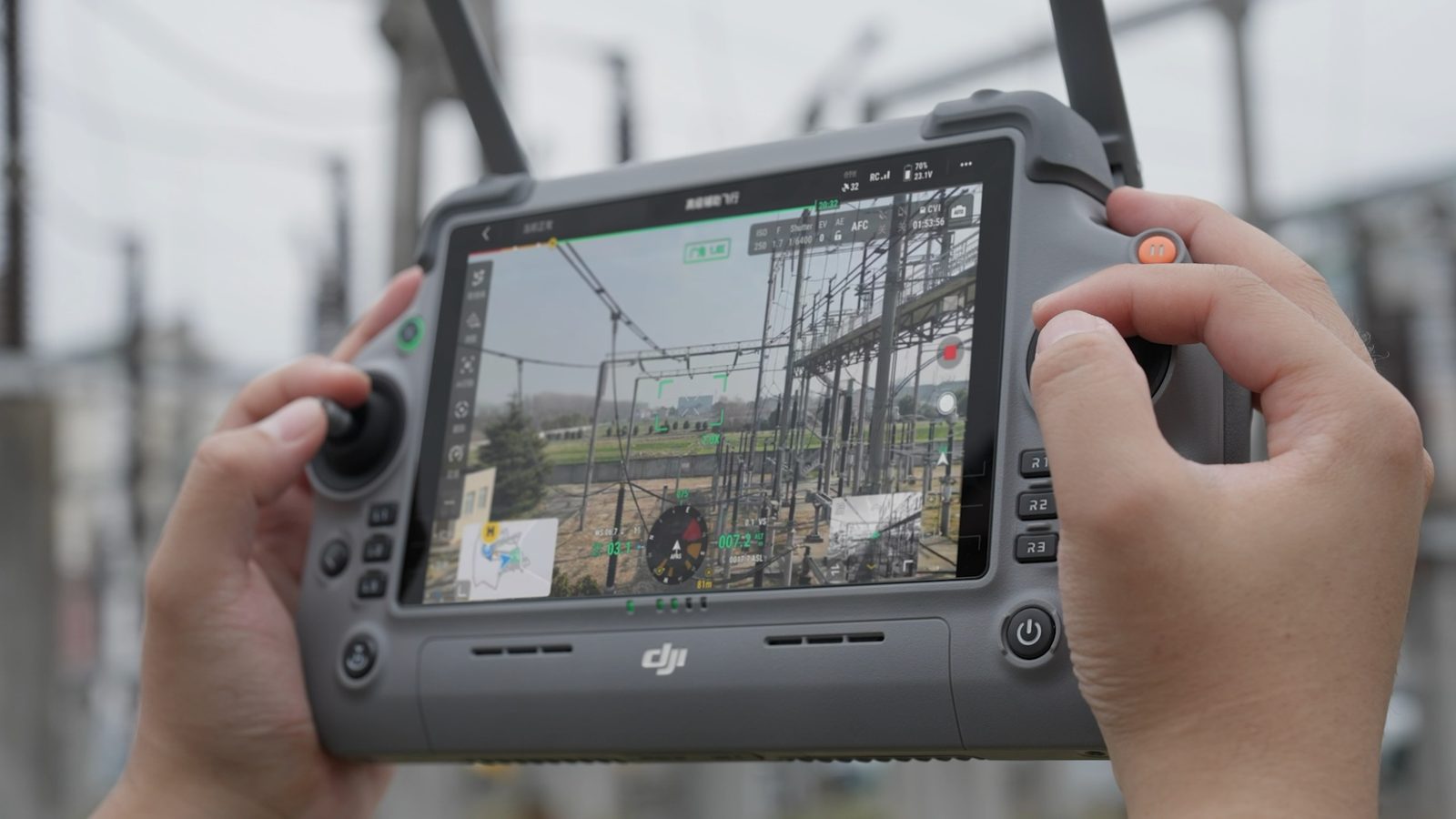 Utility technician holding a DJI controller while inspecting substation structures with a drone overhead.